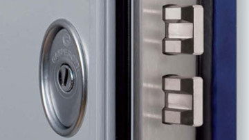 Immagine di catalogo di un dettaglio di una porta blindata per esterni di colore grigio chiaro, con serratura, cilindro e meccanismi di apertura in primo piano